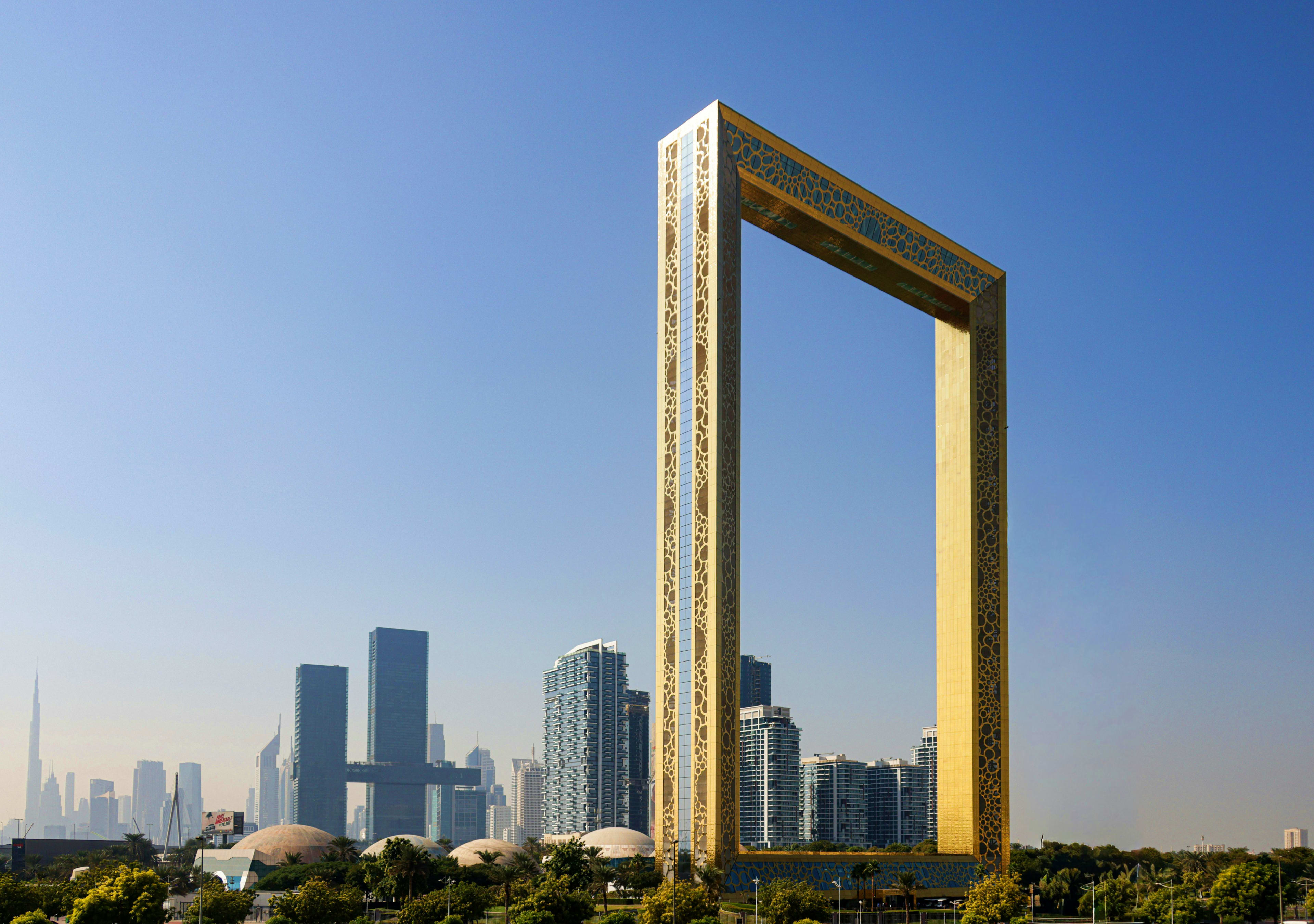 United Arab Emirates Golden Frame monument with Dubai skyline and modern skyscrapers in background under clear blue sky